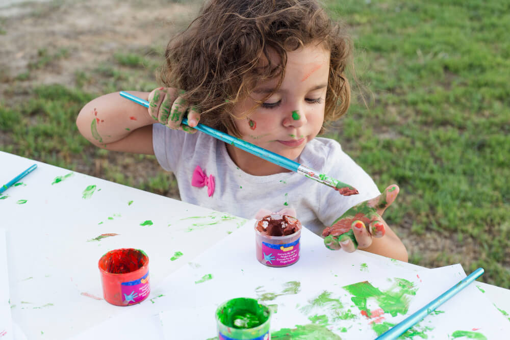 Messy little girl enjoying handprint art in the garden 